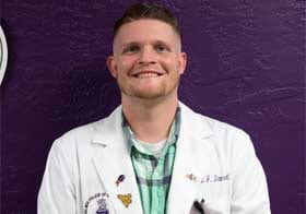 Intern of the Month John Damrath in lab coat in front of purple wall