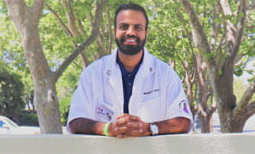 Branden Kapur smiling outdoors in white clinic coat.