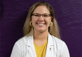 Palmer student in white lab coat smiling in front of purple clinic image.