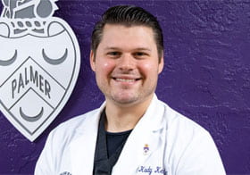 Kody Kettle smiling in white clinic coat in front of Purple wall