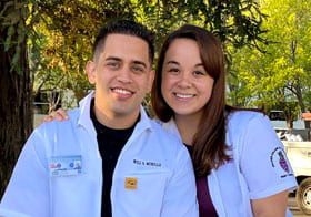 Couple in white clinic coats smiling in outdoor photo.