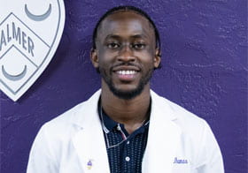 Andric Thomas in a white clinic coat in front of purple wall and Palmer crest.