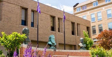 Brick wall with three busts behind purple flowers