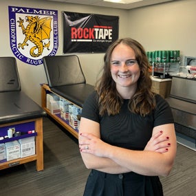 Allison David posing with arms crossed in front of Rugby flag.