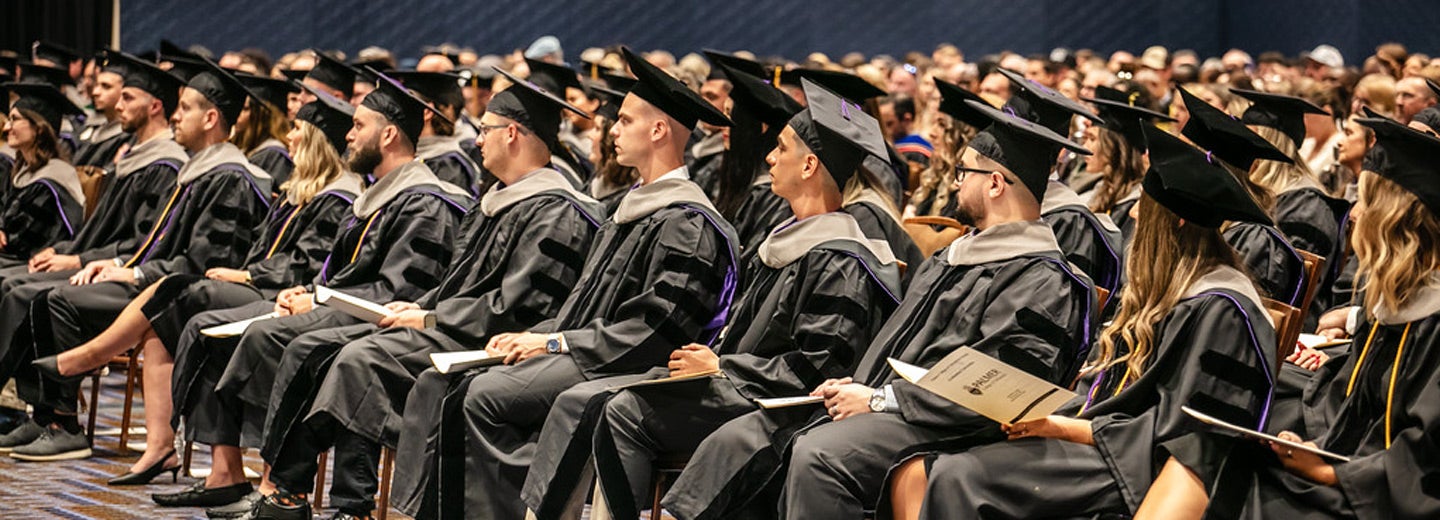 Large room of students in graduation cap and gowns.