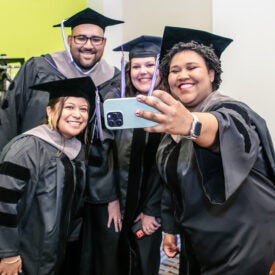 Students in graduation cap and gowns taking a selfie.