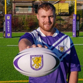 Student Cameron Dowie holding rugby ball on outside rugby field.