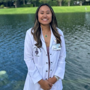 Cindy Le in white chiropractic coat in front of fountain.