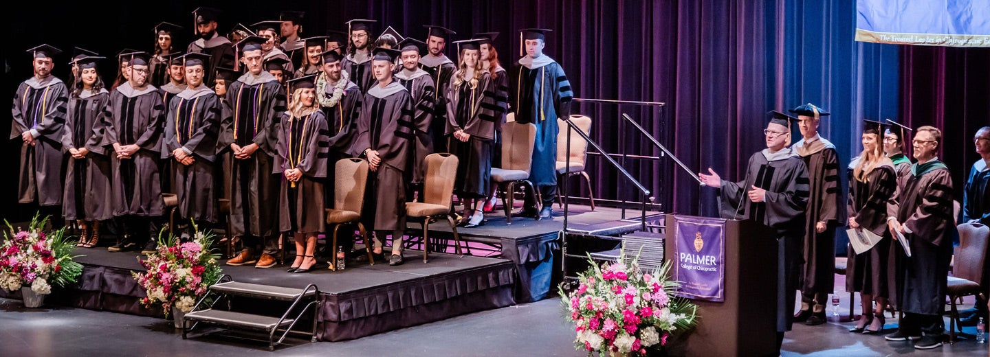 West graduation class 171 in cap and gowns watching as speaker talks at podium.