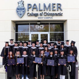 West graduation class 171 in cap and gowns standing outside the West building.